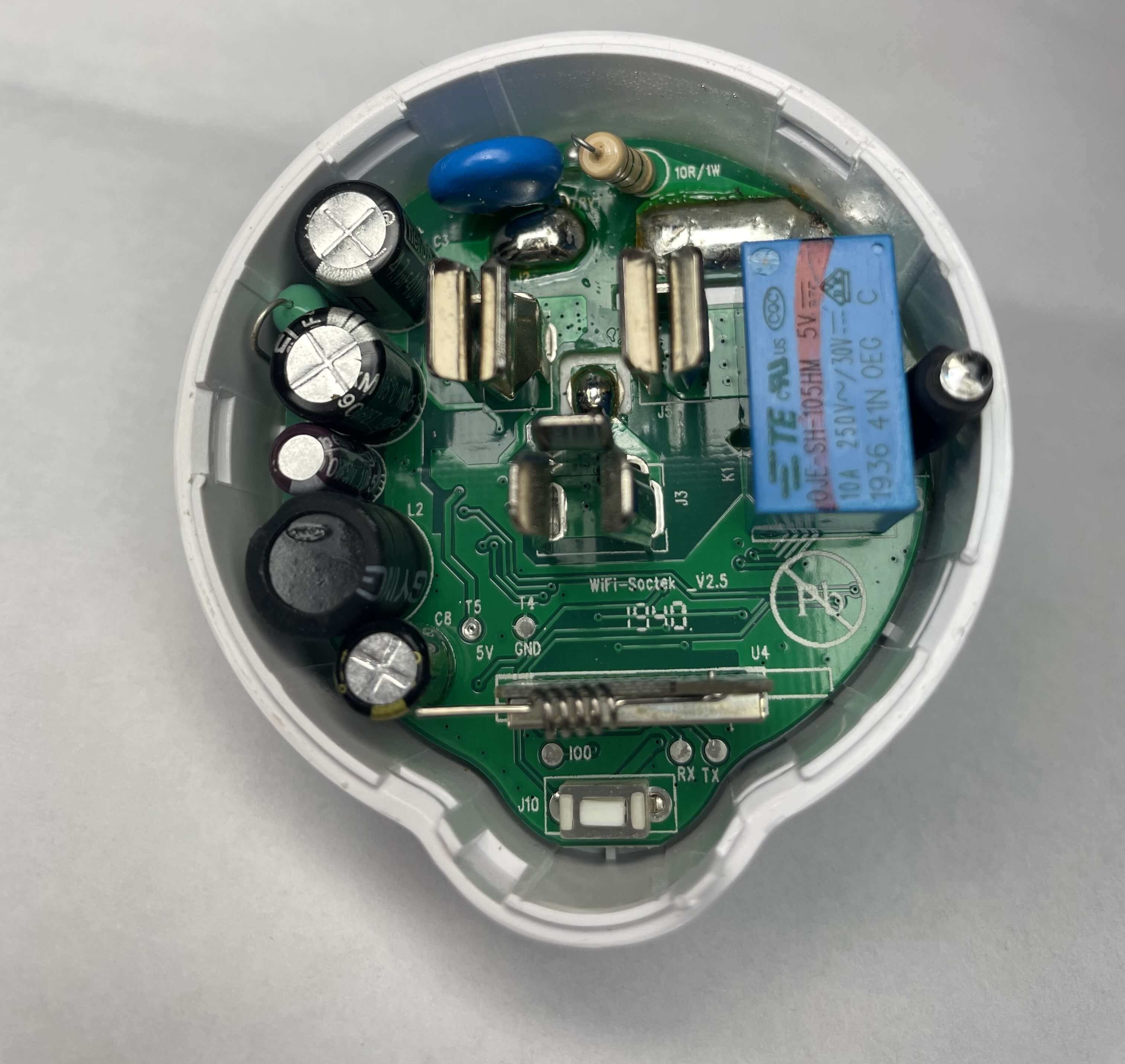 A top-down view of the Etekcity Voltson ESW01-USA-R6P&#39;s PCB. At the bottom of the PCB, there is an AI-Thinker ESP 01E module identifiable by its spring antenna. Below the ESP module, there are three test pads labeled, from left to right, as IO0, RX, and TX. Above and to the left of the ESP module, there are two test pads labeled, from left to right, as T5/5V and T4/GND.